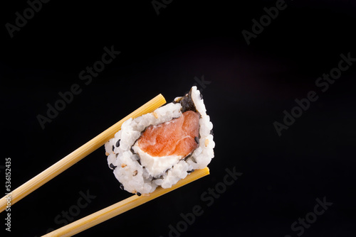 home made japanese food holding a salmon sushi with cream cheese with chopsticks isolated on black background macro closeup landscape