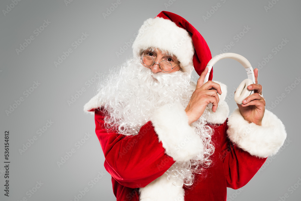 Santa claus in eyeglasses holding headphones isolated on grey.