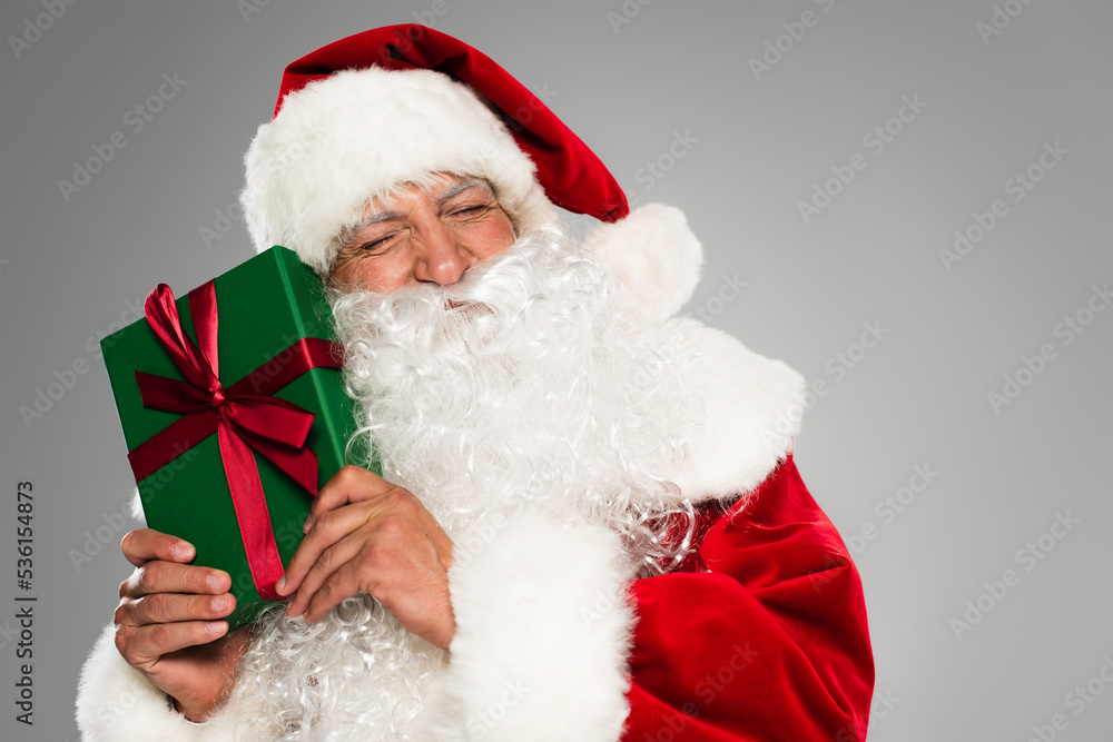 Bearded santa claus closing eyes while holding present with bow isolated on grey. Bearded santa claus closing eyes while holding present with bow isolated on grey.
