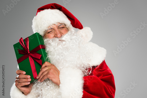 Bearded santa claus closing eyes while holding present with bow isolated on grey.