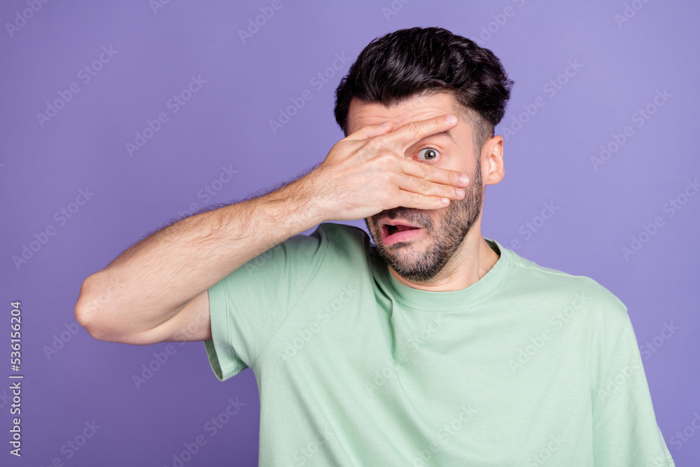 Portrait of scared stressed terrified man with brunet hairdo dressed t-shirt hiding hand cover eye isolated on purple color background Portrait of scared stressed terrified man with brunet hairdo dressed t-shirt hiding hand cover eye isolated on purple color background