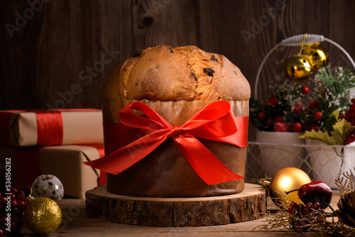 Traditional Italian Christmas Cake Panettone with red bow and festive decoration on wooden rustic background. Homemade artisan sourdough panettone is classic italian Christmas Food and Edible gift