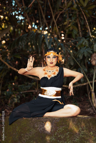 Indonesian woman sitting on the rock in a black dance costume while wearing a golden crown and golden necklace photo