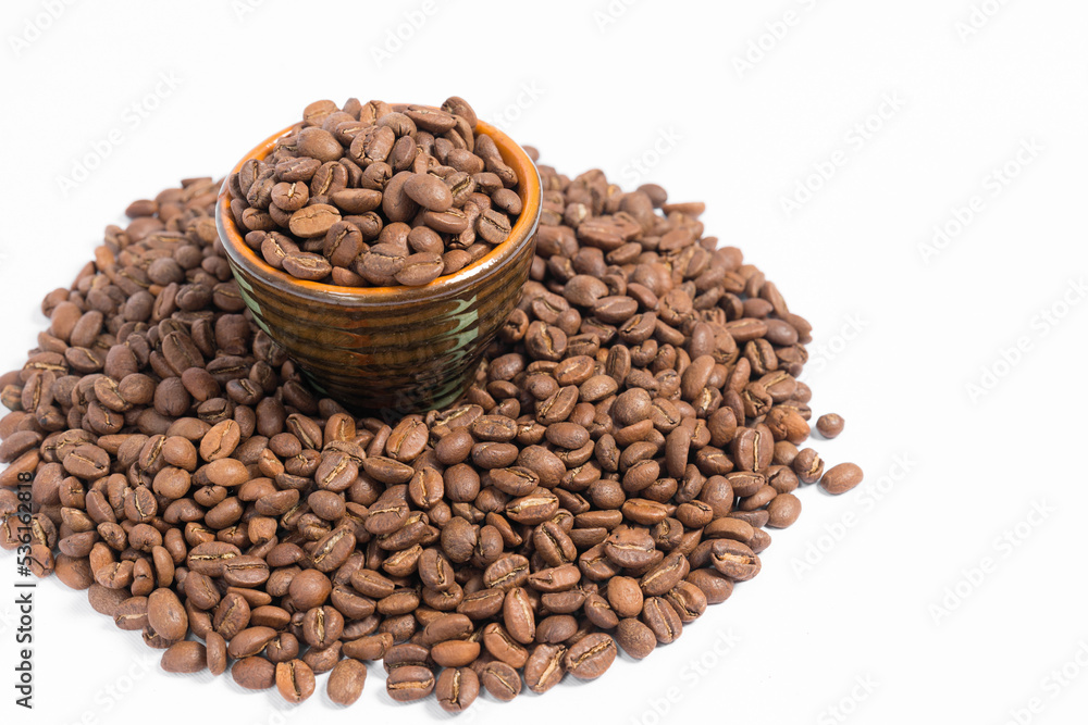 A small saucer with coffee beans stands on a pile of coffee on a white background. A small saucer with coffee beans stands on a pile of coffee on a white background.