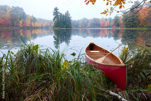 Red wood canoe on shore of a small lake with an island on a cloudy autumn morning