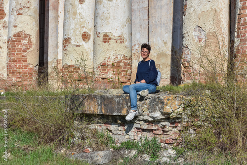 girl with glasses sits against the background of an abandoned building, an abandoned church