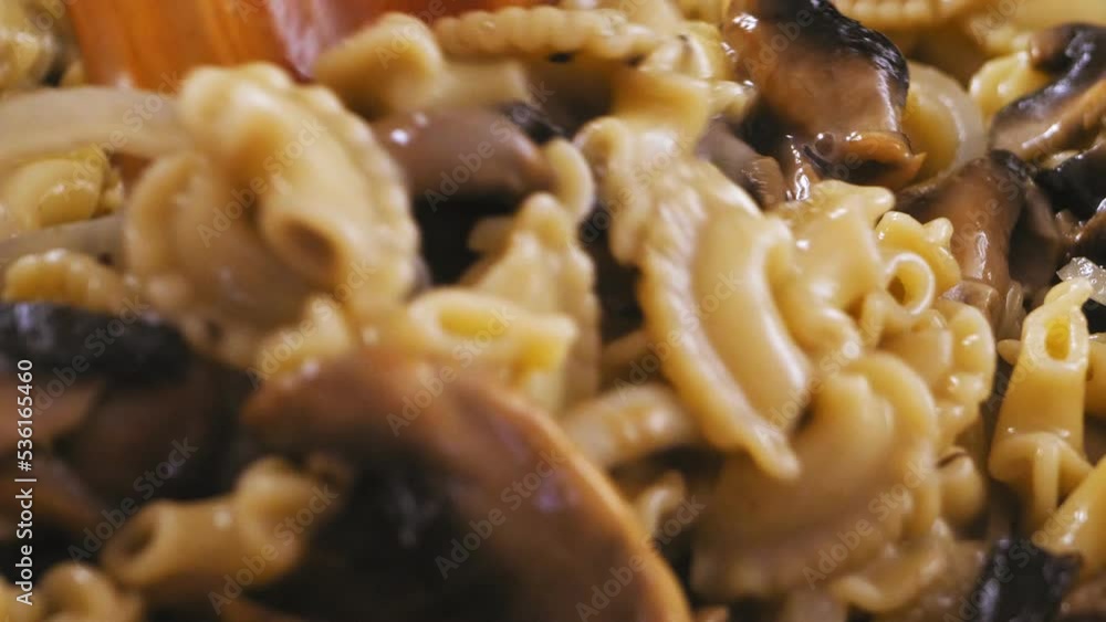 Pasta in a creamy sauce with champignons and spices is mixed with a wooden spatula. Close-up Pasta in a creamy sauce with champignons and spices is mixed with a wooden spatula. Close-up
