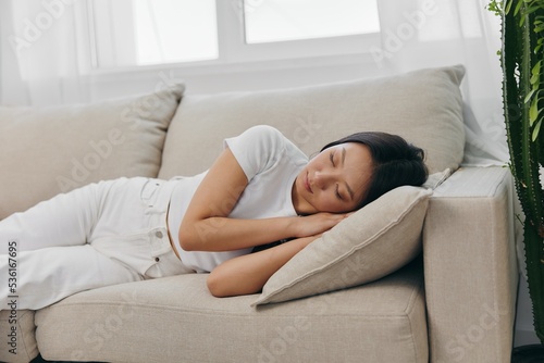 Young beautiful Asian woman sleeping on the couch at home with her eyes closed while lying on her side, resting and relaxing from stress while sleeping