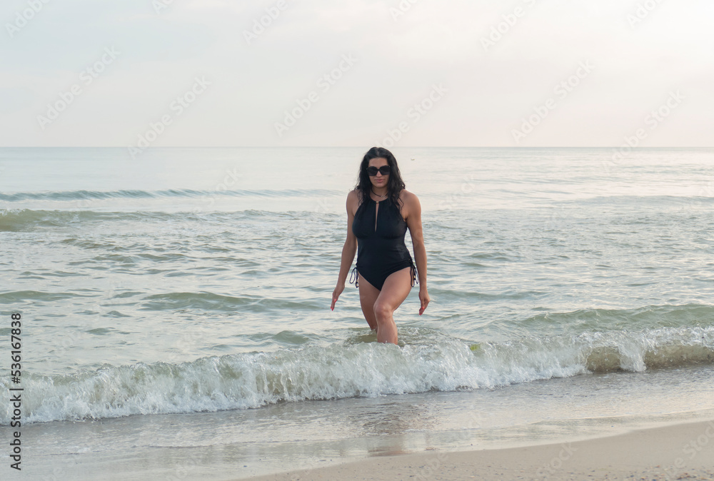 Beautiful girl with glasses on the seashore. Brunette in a black swimsuit on the beach. Beautiful girl with glasses on the seashore. Brunette in a black swimsuit on the beach.