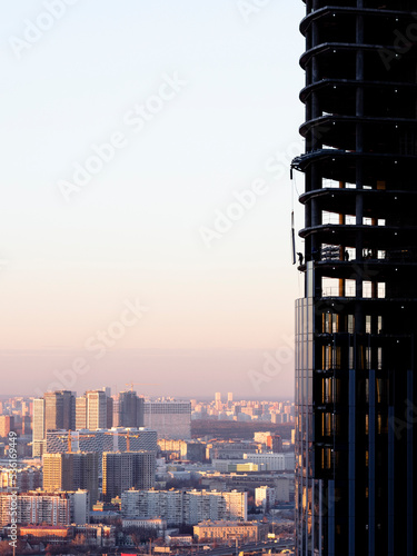 Builders install a double-glazed window of a skyscraper under construction against the background of the city and the sky