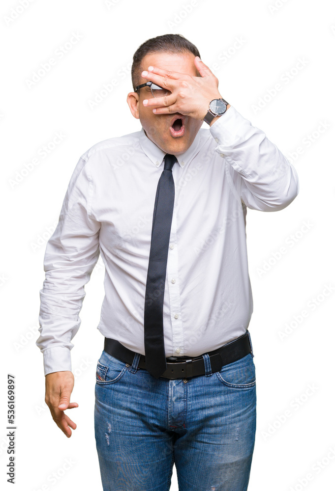 Middle age bussines arab man wearing glasses over isolated background peeking in shock covering face and eyes with hand, looking through fingers with embarrassed expression. Middle age bussines arab man wearing glasses over isolated background peeking in shock covering face and eyes with hand, looking through fingers with embarrassed expression.
