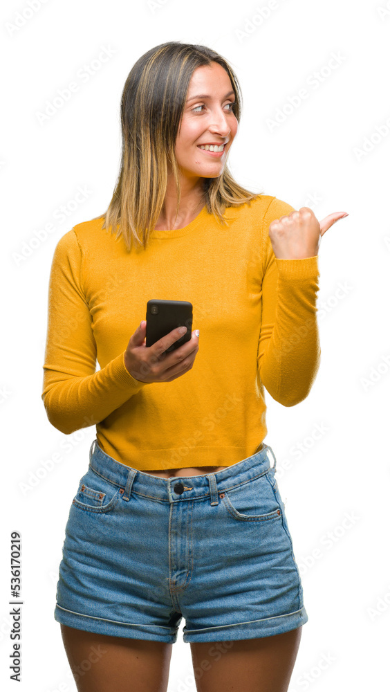 Young beautiful woman sending message using smartphone over isolated background pointing and showing with thumb up to the side with happy face smiling Young beautiful woman sending message using smartphone over isolated background pointing and showing with thumb up to the side with happy face smiling