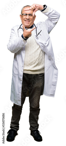 Handsome senior doctor man wearing medical coat smiling making frame with hands and fingers with happy face. Creativity and photography concept.
