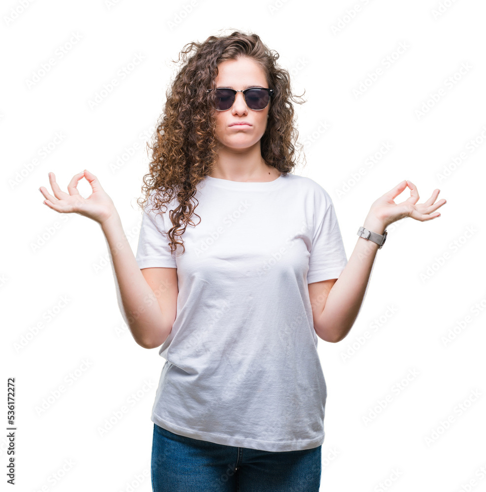 Beautiful brunette curly hair young girl wearing sunglasses over isolated background relax and smiling with eyes closed doing meditation gesture with fingers. Yoga concept. Beautiful brunette curly hair young girl wearing sunglasses over isolated background relax and smiling with eyes closed doing meditation gesture with fingers. Yoga concept.