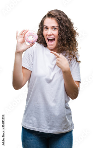 Young brunette girl eating donut over isolated background very happy pointing with hand and finger