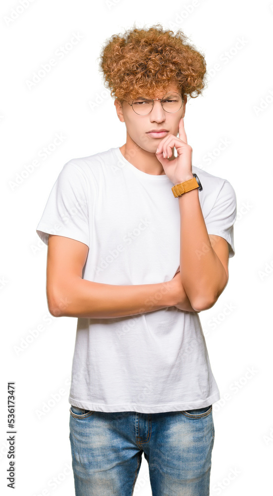 Young handsome man with afro hair wearing glasses with hand on chin thinking about question, pensive expression. Smiling with thoughtful face. Doubt concept. Young handsome man with afro hair wearing glasses with hand on chin thinking about question, pensive expression. Smiling with thoughtful face. Doubt concept.