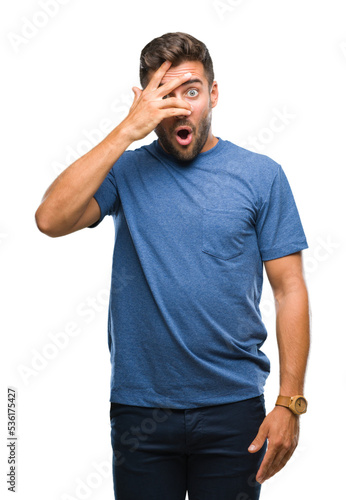 Young handsome man over isolated background peeking in shock covering face and eyes with hand, looking through fingers with embarrassed expression. © Krakenimages.com