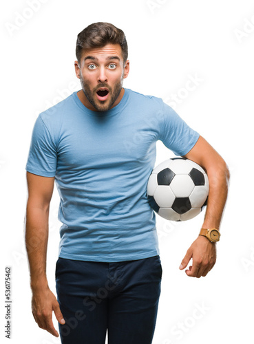 Young handsome man holding soccer football ball over isolated background scared in shock with a surprise face, afraid and excited with fear expression