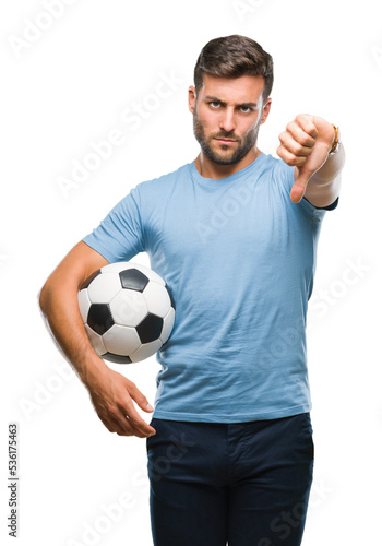Young handsome man holding soccer football ball over isolated background with angry face, negative sign showing dislike with thumbs down, rejection concept © Krakenimages.com
