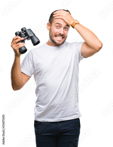 Young handsome man looking through binoculars over isolated background stressed with hand on head, shocked with shame and surprise face, angry and frustrated. Fear and upset for mistake.