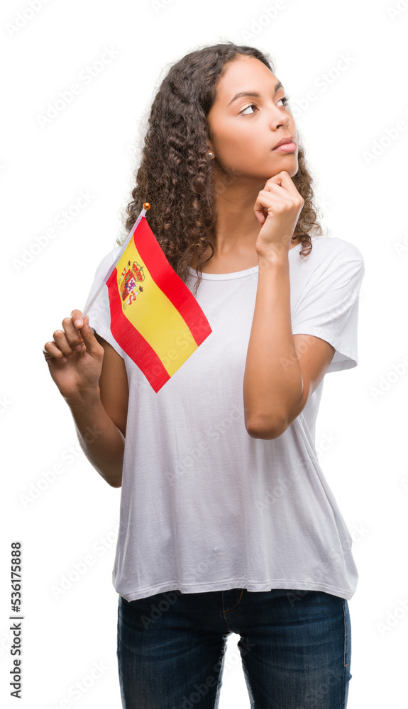 Young hispanic woman holding flag of Spain serious face thinking about question, very confused idea Young hispanic woman holding flag of Spain serious face thinking about question, very confused idea