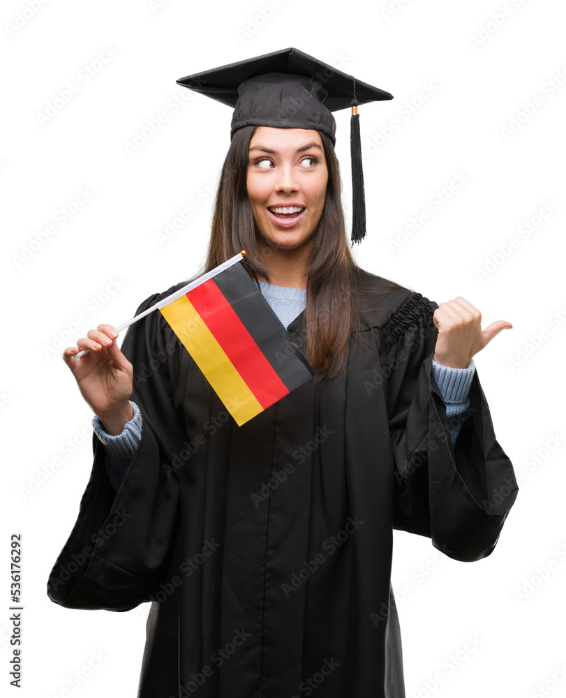 Young hispanic woman wearing graduated uniform holding flag of germany pointing and showing with thumb up to the side with happy face smiling Young hispanic woman wearing graduated uniform holding flag of germany pointing and showing with thumb up to the side with happy face smiling