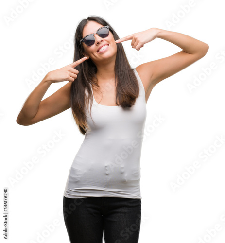 Young beautiful hispanic wearing sunglasses smiling confident showing and pointing with fingers teeth and mouth. Health concept.