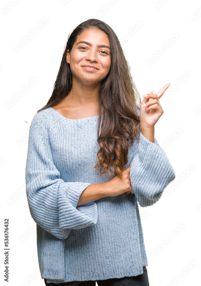 Young beautiful arab woman wearing winter sweater over isolated background with a big smile on face, pointing with hand and finger to the side looking at the camera. Young beautiful arab woman wearing winter sweater over isolated background with a big smile on face, pointing with hand and finger to the side looking at the camera.