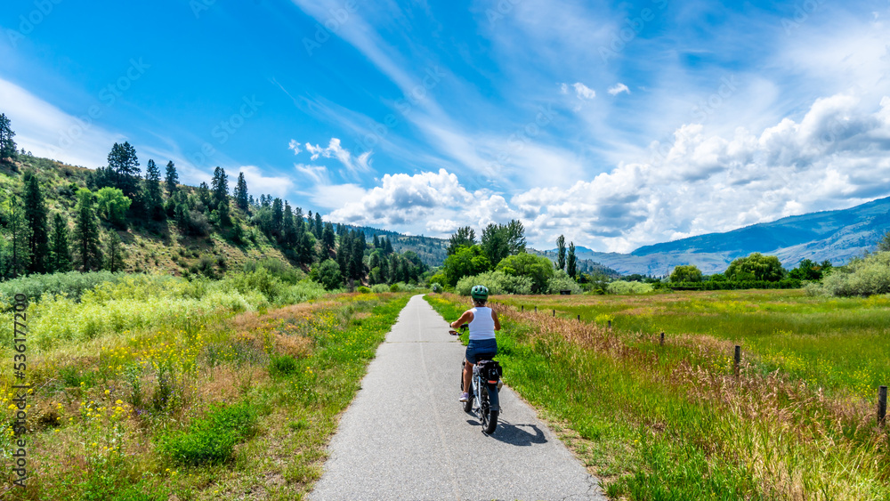 Woman on an e-bike on the trail along the Okangen River Canal between Oliver and Osoyoos in the Okanagen Valley of British Columbia, Canada Woman on an e-bike on the trail along the Okangen River Canal between Oliver and Osoyoos in the Okanagen Valley of British Columbia, Canada