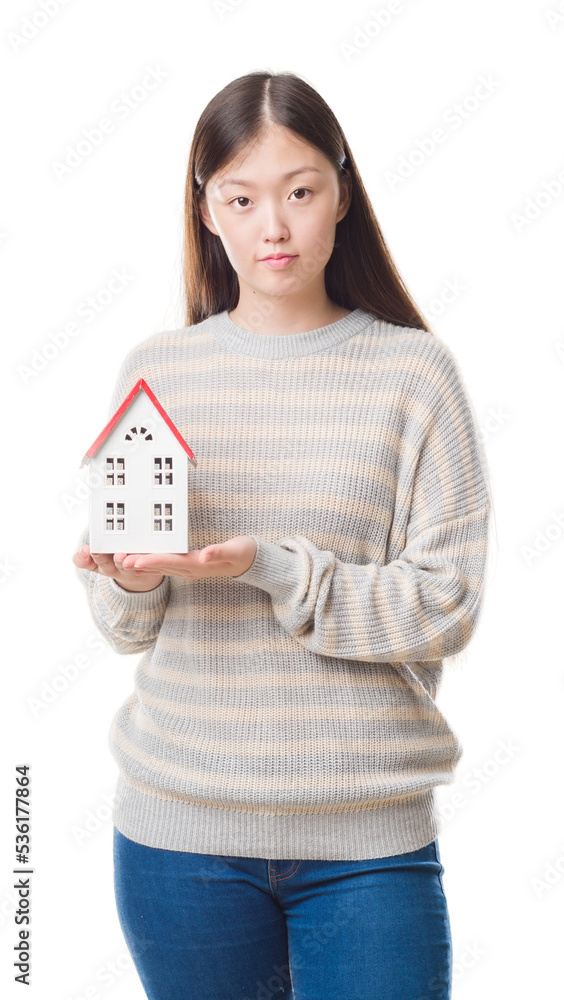 Young Chinese real state agent woman over isolated background holding house with a confident expression on smart face thinking serious Young Chinese real state agent woman over isolated background holding house with a confident expression on smart face thinking serious
