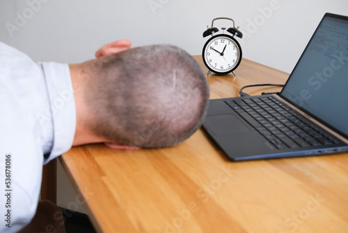 Businessman sleeping on the desk next to laptop and alarmclock
