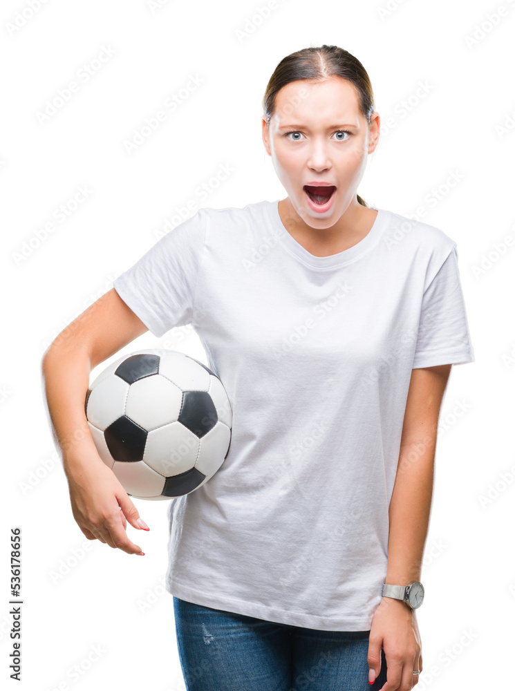 Young beautiful caucasian woman holding soccer football ball over isolated background scared in shock with a surprise face, afraid and excited with fear expression