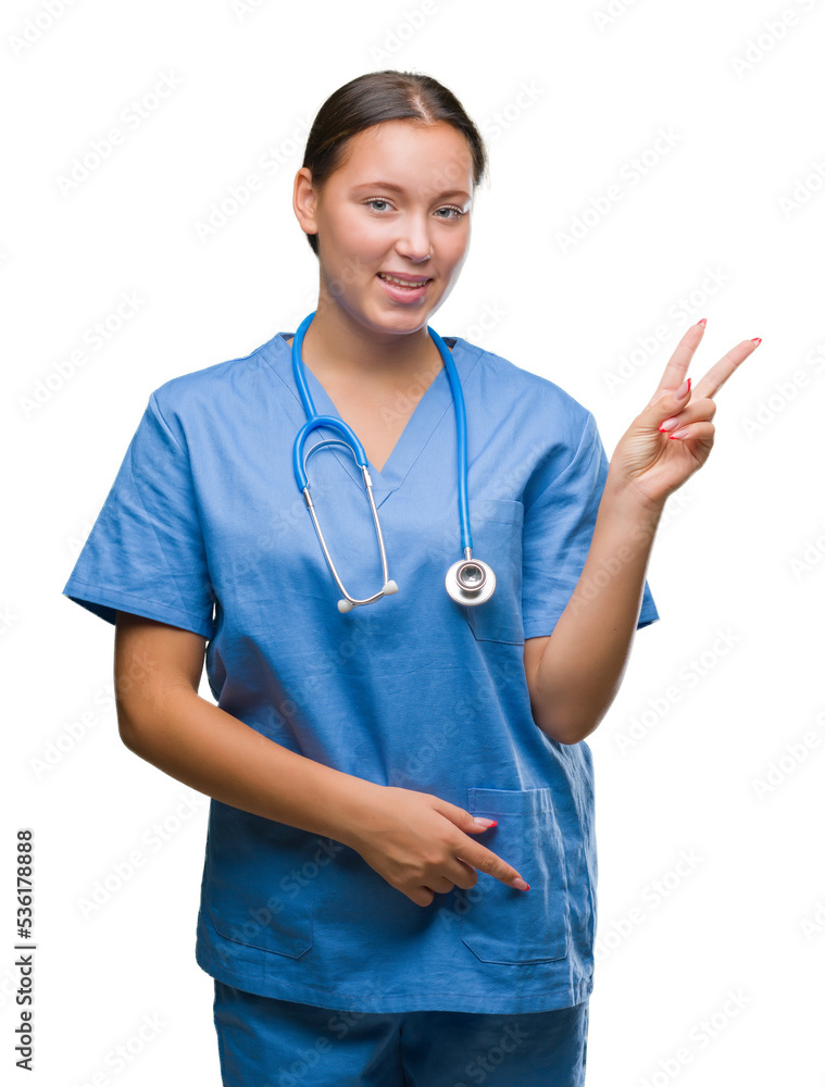 Young caucasian doctor woman wearing medical uniform over isolated background smiling with happy face winking at the camera doing victory sign. Number two.