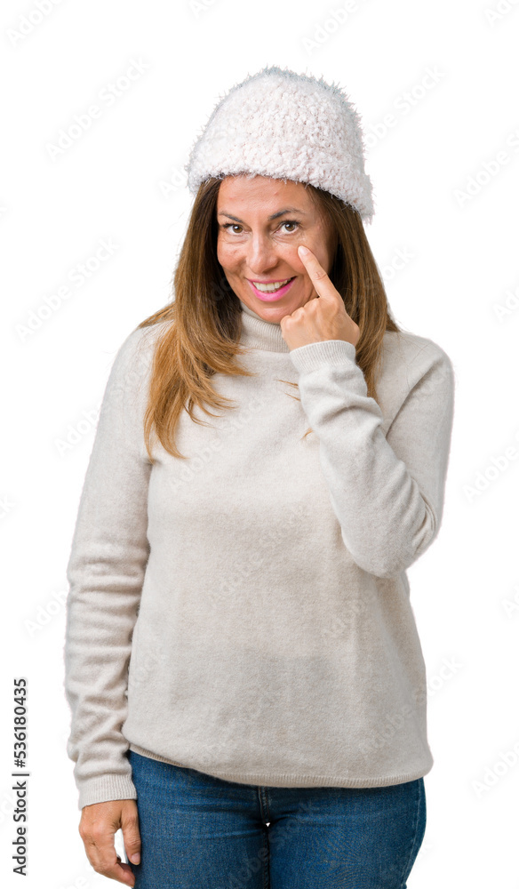 Beautiful middle age woman wearing winter sweater and hat over isolated background Pointing to the eye watching you gesture, suspicious expression Beautiful middle age woman wearing winter sweater and hat over isolated background Pointing to the eye watching you gesture, suspicious expression