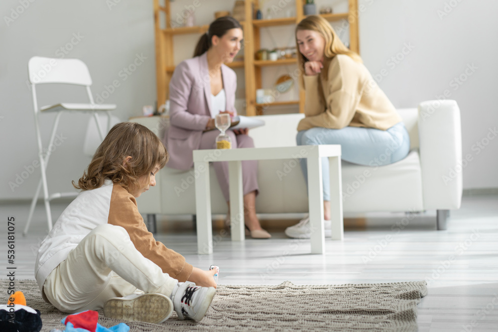 Mother with a minor son at a reception with a child psychodog. The son is sitting on a blanket on the floor playing with toys. Spacious office. Mother with a minor son at a reception with a child psychodog. The son is sitting on a blanket on the floor playing with toys. Spacious office.