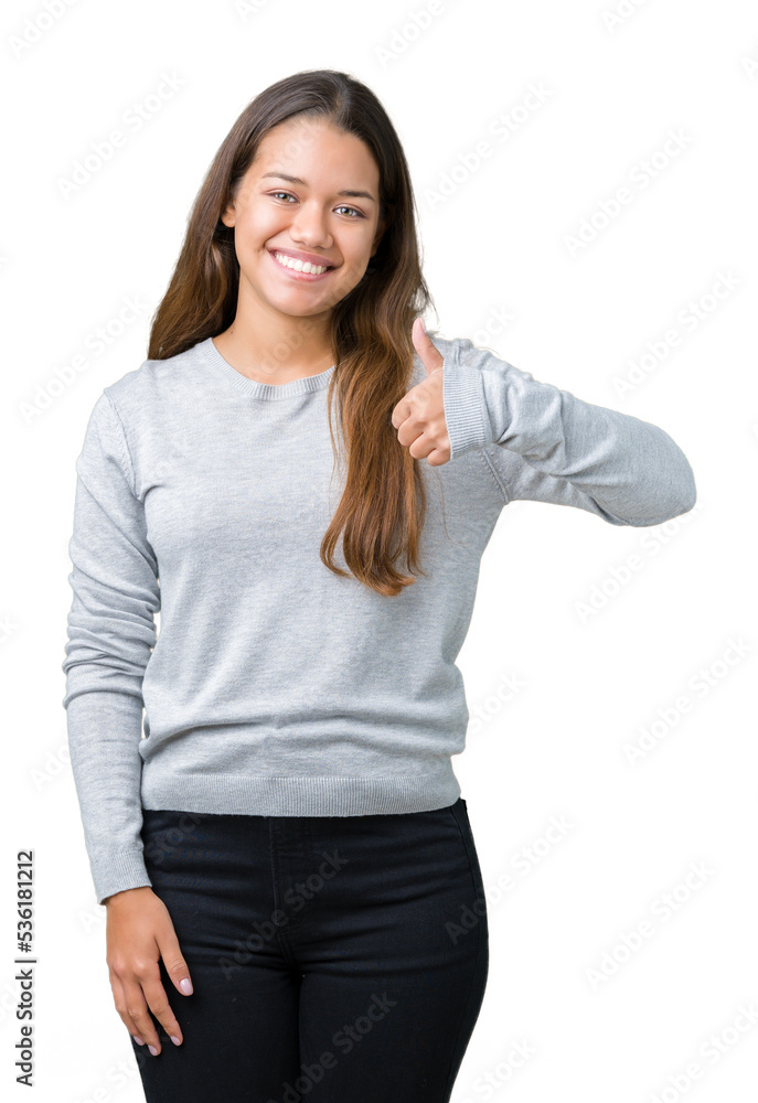 Young beautiful brunette woman wearing sweater over isolated background doing happy thumbs up gesture with hand. Approving expression looking at the camera with showing success. Young beautiful brunette woman wearing sweater over isolated background doing happy thumbs up gesture with hand. Approving expression looking at the camera with showing success.