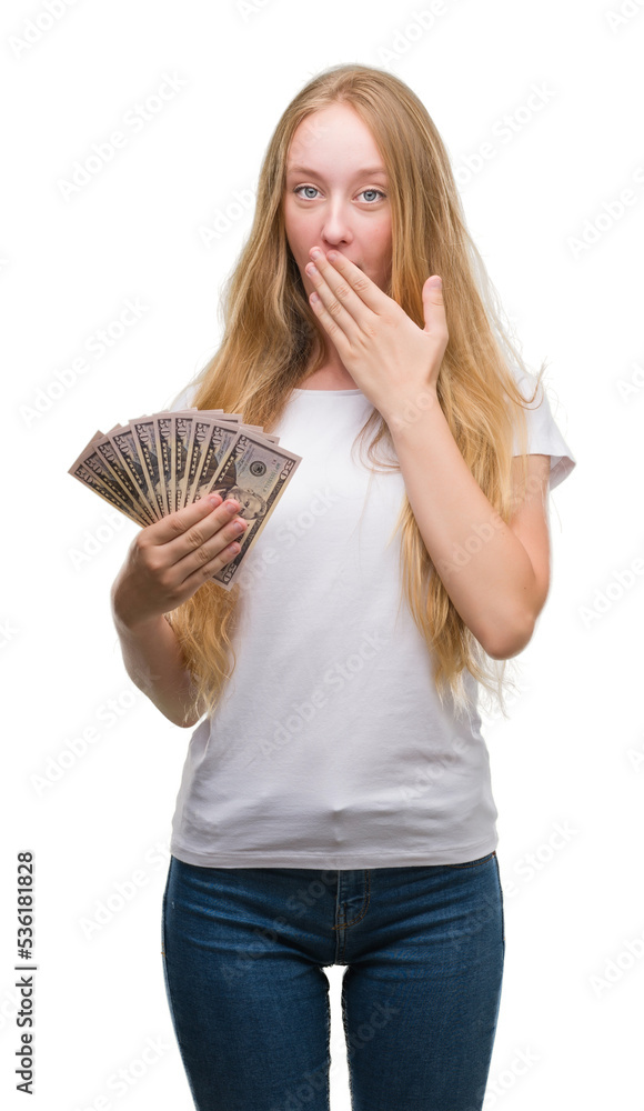 Blonde teenager woman holding dollars cover mouth with hand shocked with shame for mistake, expression of fear, scared in silence, secret concept Blonde teenager woman holding dollars cover mouth with hand shocked with shame for mistake, expression of fear, scared in silence, secret concept