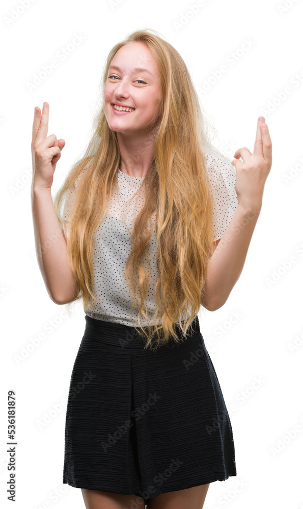 Blonde teenager woman wearing moles shirt smiling crossing fingers with hope and eyes closed. Luck and superstitious concept. Blonde teenager woman wearing moles shirt smiling crossing fingers with hope and eyes closed. Luck and superstitious concept.