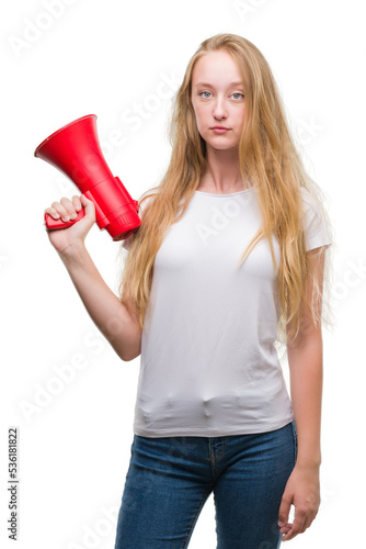 Blonde teenager woman holding megaphone with a confident expression on smart face thinking serious