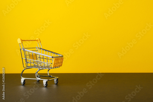 Black friday sales concept. Photo of shopping cart on tabletop yellow wall background with copyspace