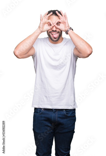 Young man wearing casual white t-shirt over isolated background doing ok gesture like binoculars sticking tongue out, eyes looking through fingers. Crazy expression.