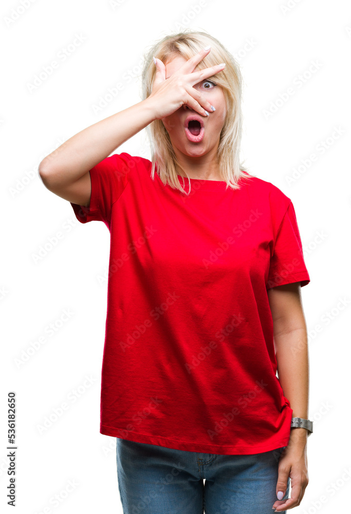 Young beautiful blonde woman wearing red t-shirt over isolated background peeking in shock covering face and eyes with hand, looking through fingers with embarrassed expression. Young beautiful blonde woman wearing red t-shirt over isolated background peeking in shock covering face and eyes with hand, looking through fingers with embarrassed expression.
