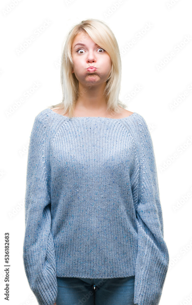 Young beautiful blonde woman wearing winter sweater over isolated background puffing cheeks with funny face. Mouth inflated with air, crazy expression. Young beautiful blonde woman wearing winter sweater over isolated background puffing cheeks with funny face. Mouth inflated with air, crazy expression.