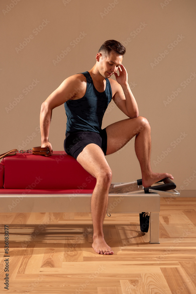 Obraz premium Fit man doing a lunge stretch yoga pilates exercise to strengthen and tone his muscles using a reformer in a gym