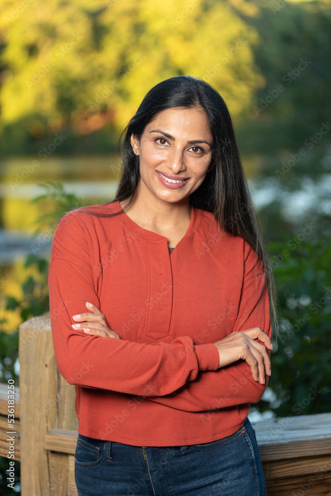 Beautiful Asian Indian woman wearing jeans and a red sweater by a lake