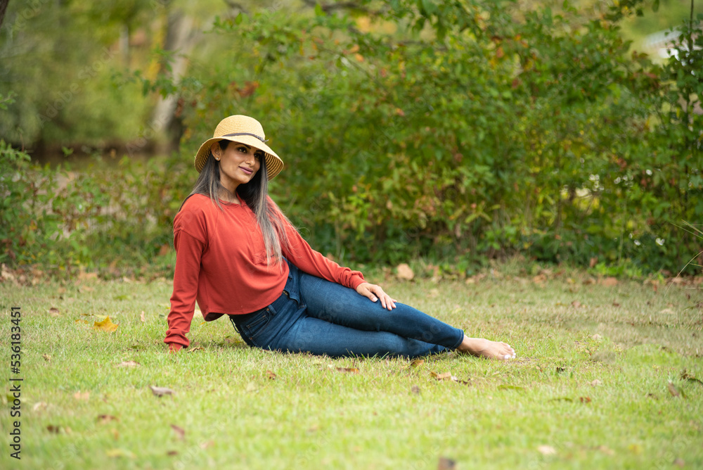 Beautiful Asian Indian woman in jeans and red sweater sitting under a tree. Beautiful Asian Indian woman in jeans and red sweater sitting under a tree.