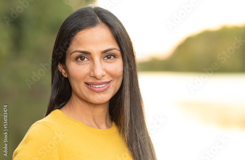 Beautiful Asian Indian woman in yellow sweater by a lake. 