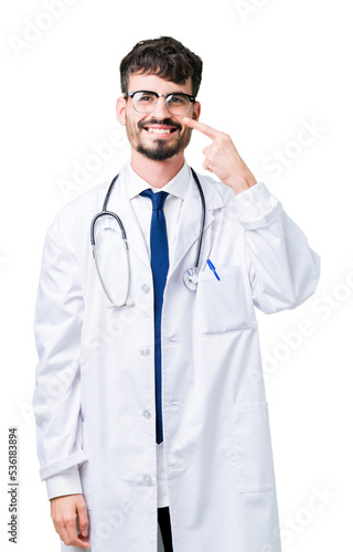 Young doctor man wearing hospital coat over isolated background Pointing with hand finger to face and nose, smiling cheerful © Krakenimages.com