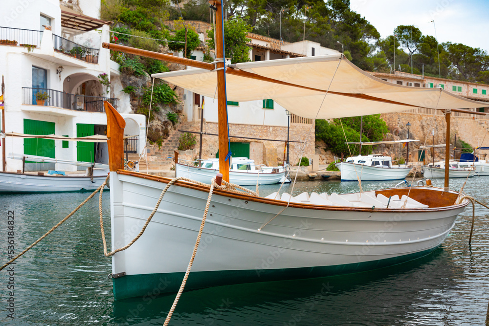 Llaut (tradicional barco de pesca de las Islas Baleares) en el puerto pesquero de Cala Figuera, en el este de la isla de Mallorca (Islas Baleares, España). Al fondo pueden verse los típicos "escars". - obrazy, fototapety, plakaty 