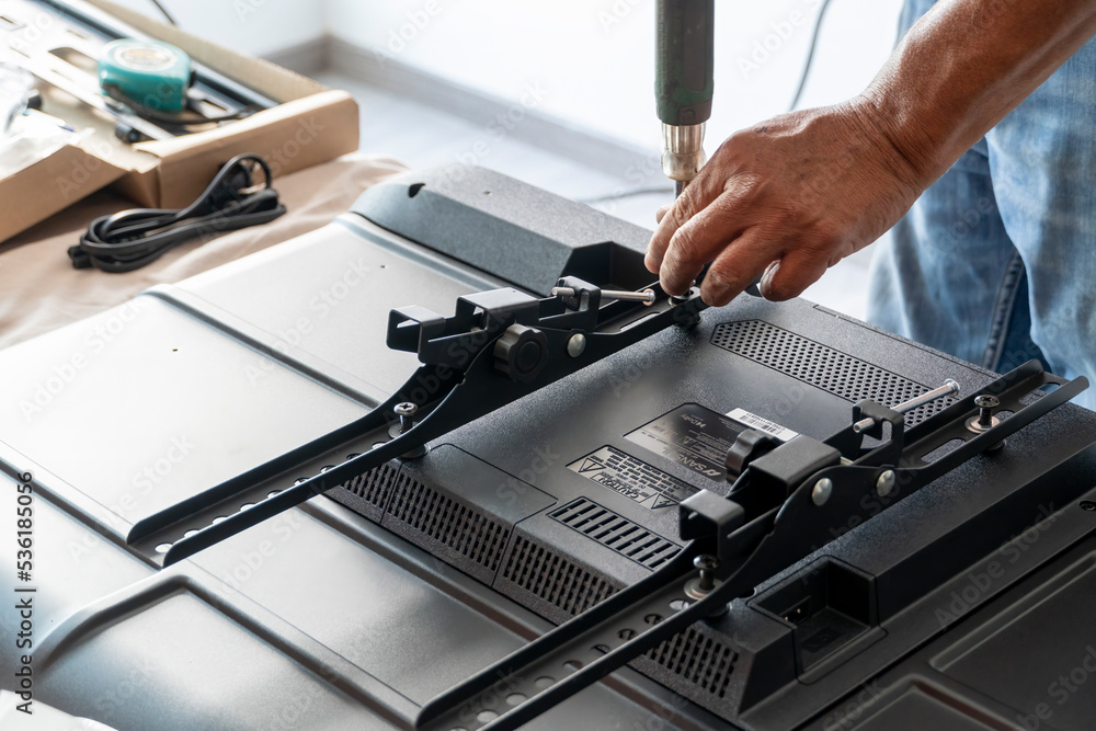 man installing the wall base for the television, it is a smart tv, adjusting with screwdriver man installing the wall base for the television, it is a smart tv, adjusting with screwdriver